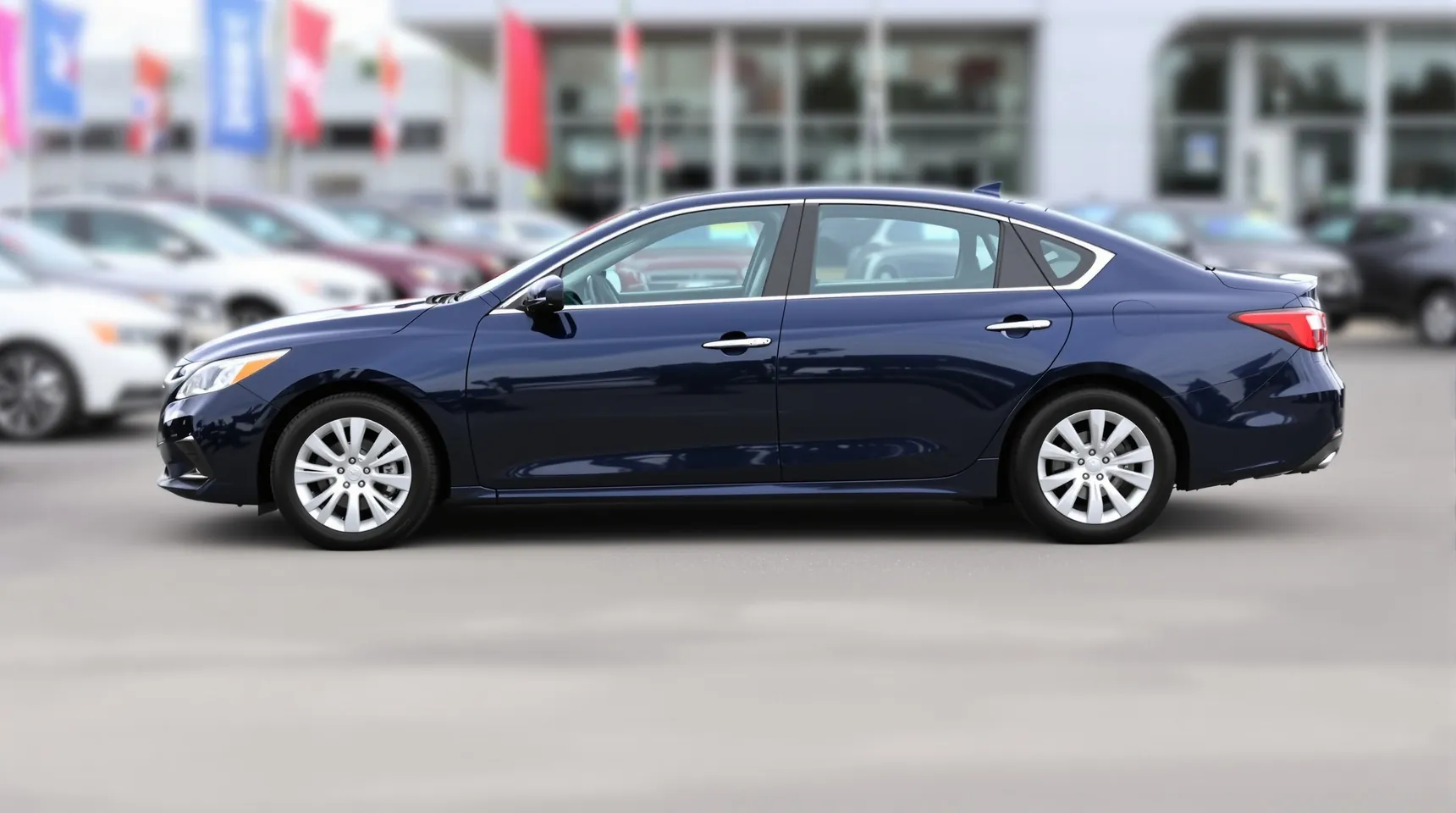 A dark blue sedan on a car dealership lot with flags and other cars behind
