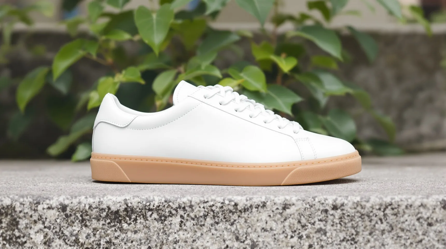 A white leather sneaker with a gum sole on a concrete step outdoors